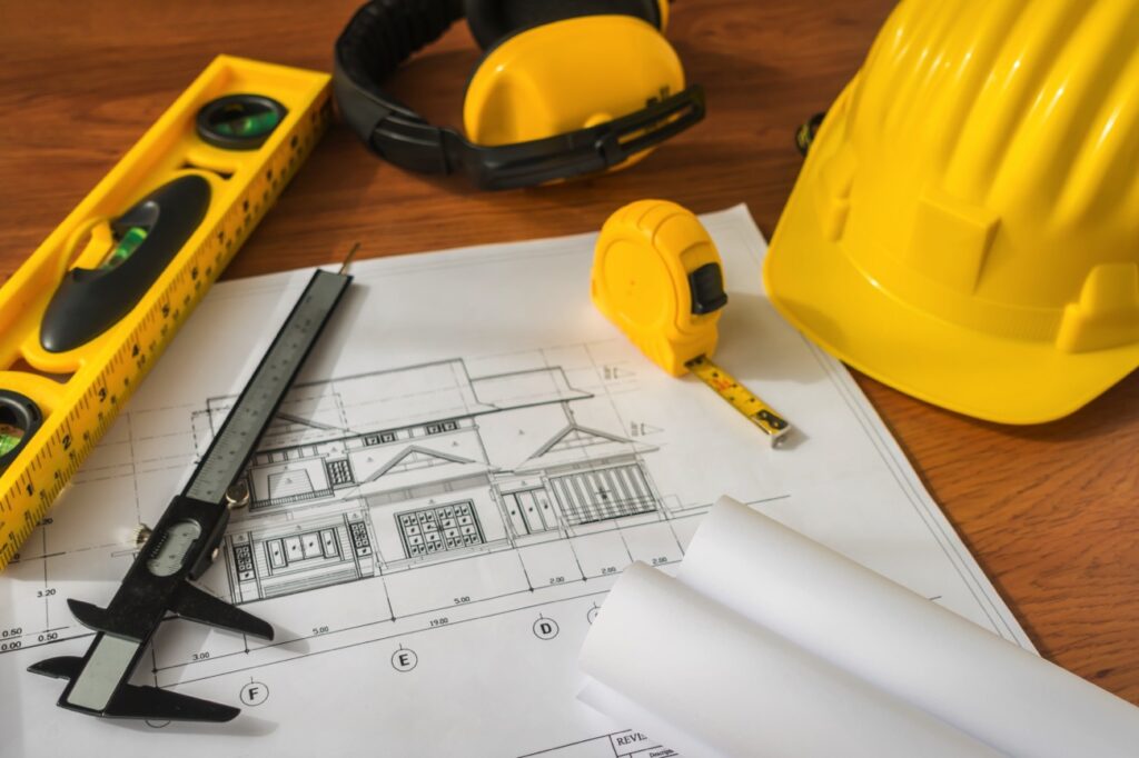 Zdjęcie przedstawia przedmioty budowlane, kask i narzędzia pomiarowe.